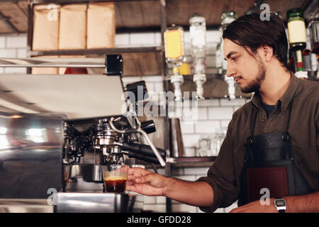 Vista laterale dei maschi di barista preparare l'espresso presso la caffetteria. Giovane uomo in grembiule di bollitore per caffè con caffè presso la caffetteria. Foto Stock