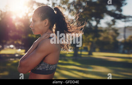 Vista laterale colpo di montare la giovane donna in piedi in un parco. Focalizzato giovane atleta femminile in piedi all'aperto sulla giornata di sole. Spazio copia ri Foto Stock