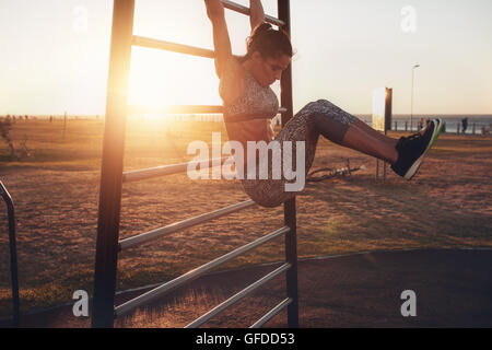 Candide colpo di vero e sano montare donna eseguendo appesi solleva la gamba sul fitness all'aperto dalla stazione di tramonto al lungomare. Foto Stock