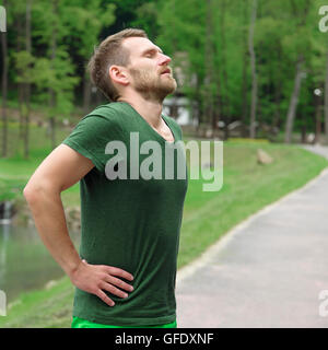 Runner in appoggio stanco ed esausto dopo l'esecuzione. Jogging uomo prendendo una pausa durante il corso di formazione esterno in sulla strada di montagna. Foto Stock