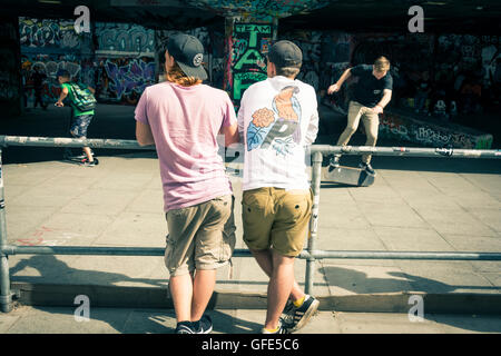 Due giovani uomini guardano skateboarders facendo trucchi sotto il Royal Festival Hall di Southbank Centre di Londra, Regno Unito Foto Stock