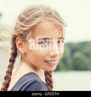 Ritratto di giovane ragazza felice con trecce guardando nella telecamera. Calda tonalità di colore immagine Foto Stock