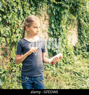 Carino young teen girl disegnare o scrivere i suoi pensieri in notebook nei pressi di antiche rovine coperte con wild grapevine. Estate italiano Foto Stock