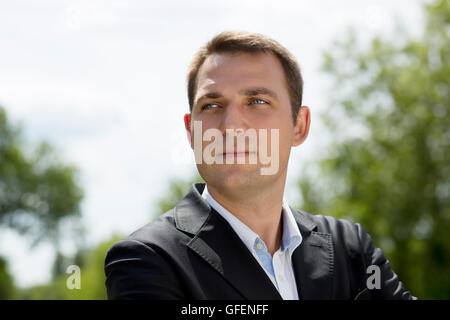 Close-up ritratto di un giovane uomo di affari in un abito scuro e camicia bianca sullo sfondo della città di estate Foto Stock