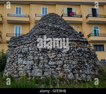 Una tradizionale casa trulli è visibile nella parte anteriore di un moderno blocco di appartamenti a Martina Franca, Puglia, Italia Foto Stock