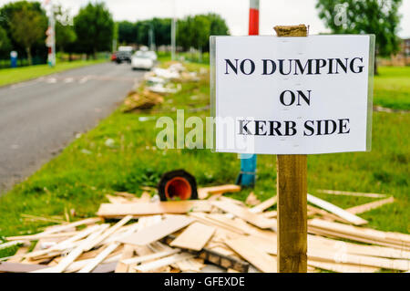 Un segno su un orlo di erba avviso di persone non a discarica di rifiuti su cordolo laterale, con un sacco di scartato legno, spazzatura e altri elementi che inquinano il terreno. Foto Stock