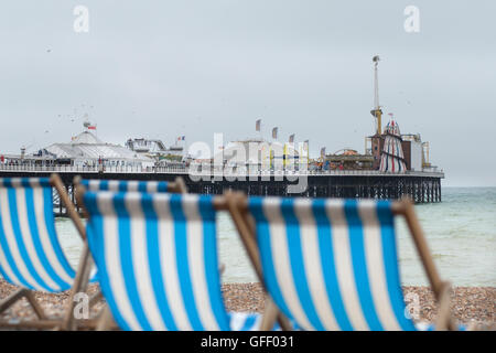 Blu e bianca a strisce sedie a sdraio che si affacciano sul mare e il Brighton Pier su un nuvoloso giorno grigio in Sussex Foto Stock