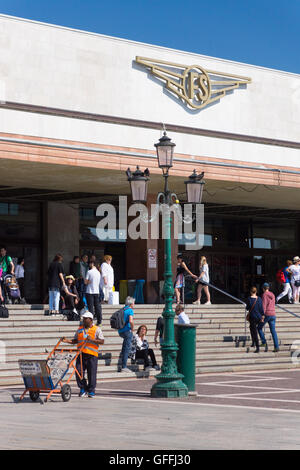 I viaggiatori che viaggiano in treno camminano dentro e fuori dall'ingresso della stazione ferroviaria di Santa Lucia, Venezia, Italia. Il logo qui sopra recita FS (Ferrovie dello Stato Italiane) Foto Stock