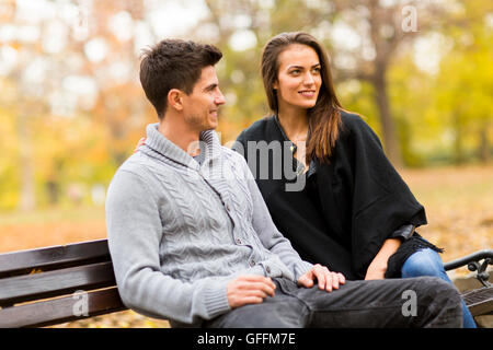 Giovane coppia sorridente seduto su un banco di lavoro in autunno park Foto Stock