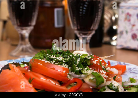 I Verdi e i semi di sesamo in una insalata di verdure con pomodori, cetrioli e cipolle su uno sfondo di bicchieri di vino rosso Foto Stock