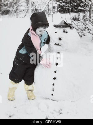 Vintage anni cinquanta la mano fotografia oscurata, giovane ragazza in doposci costruire un pupazzo di neve, STATI UNITI D'AMERICA Foto Stock