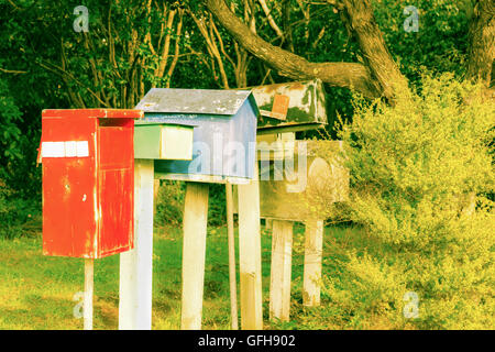 Reto stile vecchia immagine letterbox line up differenti colori rosso, verde e blu circondata da alberi e boccola Foto Stock