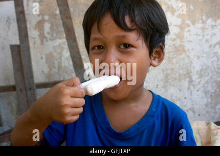 Un giovane ragazzo è mangiare un gelato bar in una delle baraccopoli in Kampong Cham, Cambogia. Foto Stock