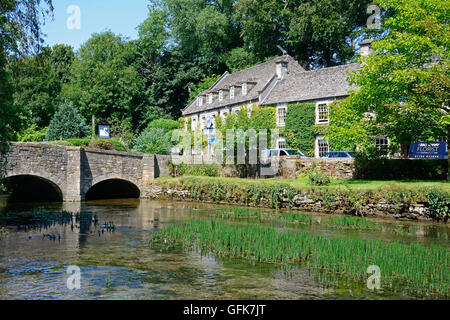 Vista lungo il Fiume Coln verso il ponte di pietra con la Swan Hotel verso la parte posteriore, Bibury, Cotswolds, Gloucestershire, Inghilterra, Foto Stock