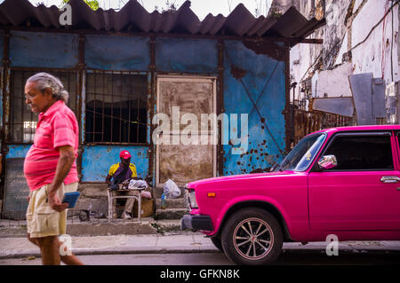L'Avana, Cuba su dicembre 23, 2015: Un uomo cammina giù per una strada in Centro Habana con la sua maglietta che corrisponde al colore di un rosa oldtim Foto Stock