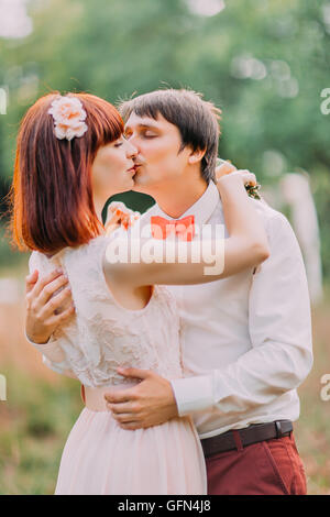 Lo sposo baci sposa teneramente tenendo la sua vita mentre stanno nel parco Foto Stock