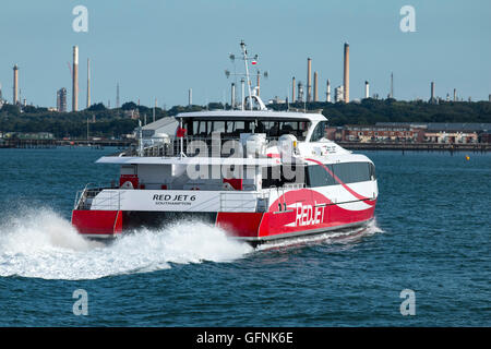 Imbuto Rosso di traghetto veloce Jet rosso 6 lasciando Town Quay, Southampton en route a Cowes Isola di Wight. Il Fawley raffineria di petrolio è in background Foto Stock
