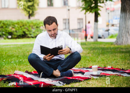Bel giovane imprenditore libro lettura sdraiati nel parco Foto Stock
