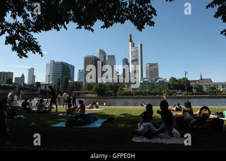 Le persone godono di estate sul terrapieno Schaumainkai in Frankfurt am Main, Hesse, Germania, con moderni grattacieli del Bankenviertel (distretto bancario) sorto in background. Foto Stock