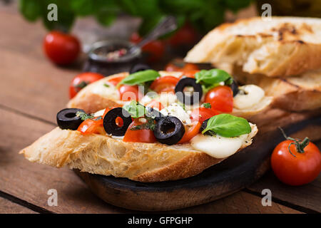 Bruschetta con pomodori, mozzarella, olive e pesto di basilico Foto Stock