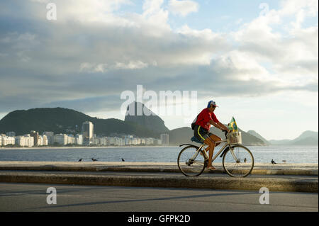 RIO DE JANEIRO - MARZO 20, 2016: un uomo brasiliano giostre di una bicicletta con una bandiera brasiliana nel cesto lungo la strada sulla spiaggia. Foto Stock