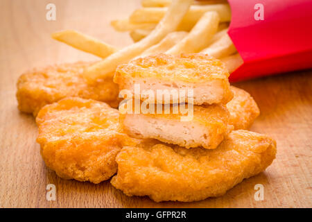 Bambini Bambino marrone oro pepite di pollo e patatine fritte pasto su uno sfondo di legno Foto Stock