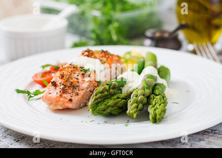 Di salmone al forno guarnito con asparagi e pomodori con erbe aromatiche Foto Stock
