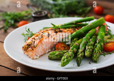 Di salmone al forno guarnito con asparagi e pomodori con erbe aromatiche Foto Stock