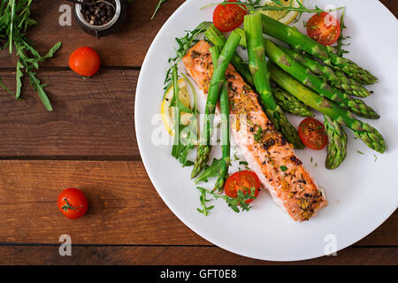 Di salmone al forno guarnito con asparagi e pomodori con erbe aromatiche. Vista superiore Foto Stock