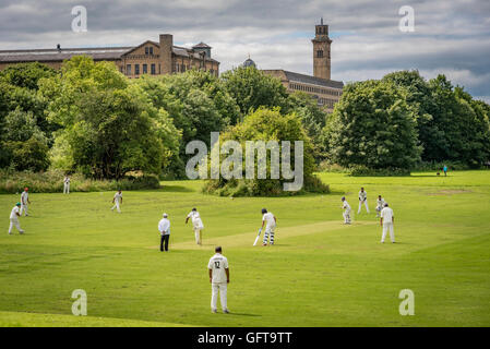 Una partita di cricket sotto la Nuova Cartiera di Saltaire nel West Yorkshire. Un NHS stabilimento accanto al fiume Aire. Foto Stock