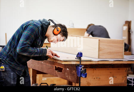 Un workshop di mobili un uomo segnando un pezzo di legno con una matita Foto Stock