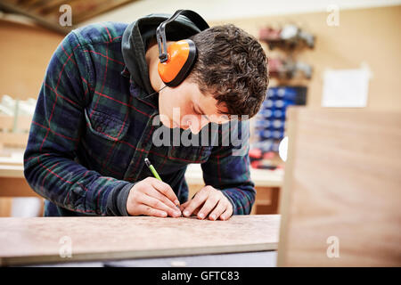 Un workshop di mobili un uomo segnando un pezzo di legno con una matita Foto Stock