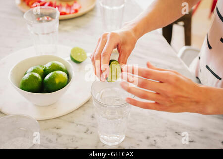 Una donna la spremitura di Limette fresche in un bicchiere di acqua Foto Stock