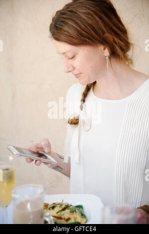 Ritratto di una donna con lunghi capelli auburn in una treccia guardando il suo telefono cellulare Foto Stock