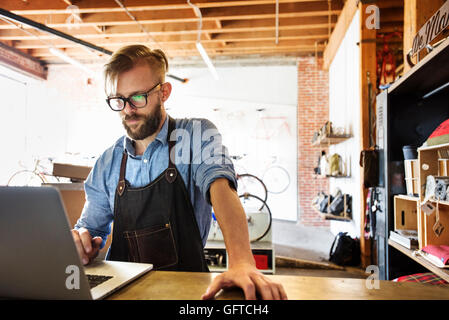 Un uomo in un negozio di riparazione di biciclette usando un computer portatile che esegue un business Foto Stock