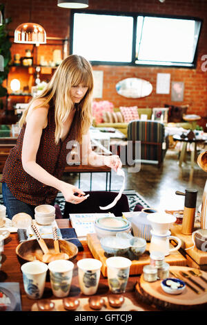 Donna in piedi in un negozio di disporre della merce su un tavolo Foto Stock
