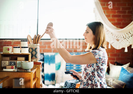 Giovane donna in un negozio di immissione di un cucchiaio di legno in un vaso e tenendo premuto uno scanner di codici a barre Foto Stock