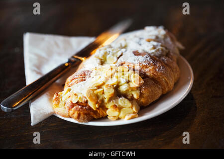 Una pasticceria fresca di un croissant alle mandorle in un posto con un coltello Foto Stock
