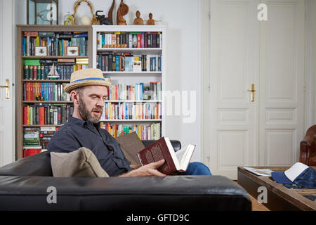 Hipster con hat la lettura di un libro a casa in un vecchio edificio con uno scaffale in background Foto Stock