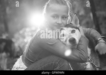 Foto in bianco e nero di una ragazza che abbraccia il suo cane husky sullo sfondo di foglie in primavera. Foto Stock