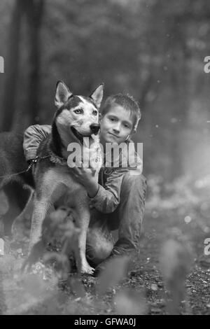 Bianco nero photo boy e il suo cane husky sullo sfondo di foglie in primavera. Foto Stock