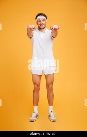 Allegro fitness giovane uomo in piedi e a fare gli esercizi con pesi su sfondo giallo Foto Stock