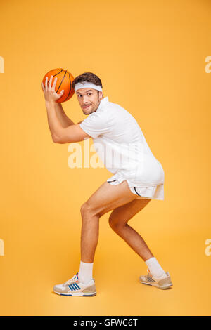 Ritratto di un bel giovane uomo concentrato giocare a basket isolata su uno sfondo arancione Foto Stock