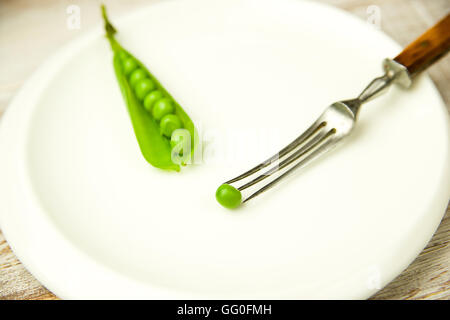 Green pea pod e la forcella sulla piastra bianca. Foto Stock