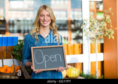 Sorridente personale femminile tenendo aperte segno bordo nel super mercato Foto Stock