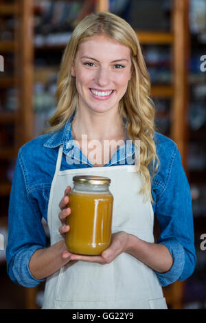 Sorridente personale femminile tenendo un vasetto di miele nel supermercato Foto Stock