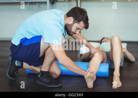 Fisioterapista facendo terapia della gamba per una donna usando il rullo di schiuma Foto Stock