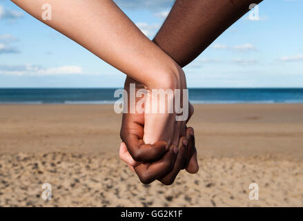 Tenere la mani giovane close up maschile femminile multiculturale di razza mista il mare e la sabbia insieme amore simbolo di pace Foto Stock