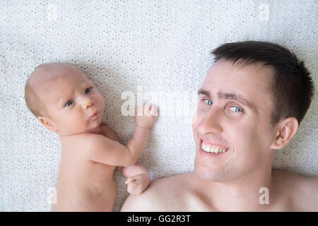 Ritratto di giovane uomo felice e il neonato carino babe giacente su coltre bianca e guardando la fotocamera. Sorridente padre caucasici in posa Foto Stock