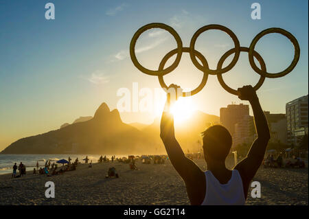 RIO DE JANEIRO - MARZO 05, 2016: atleta detiene anelli olimpici sopra tramonto vista dello skyline della citta' di due fratelli di montagna a Ipanema. Foto Stock